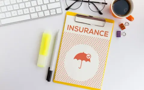 Dokument "Insurance" z parasolką, klawiatura, okulary, kawa. Planowanie ubezpieczenia zdrowotnego bez pracy.