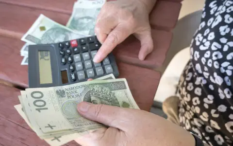 Ręce liczą banknoty 100 zł przy kalkulatorze. Może to być pomocne przy analizie nowych zasad przejścia na emeryturę tabela.