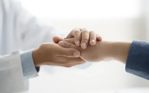 Lekarz w białym kitlu trzyma dłoń pacjenta, okazując wsparcie. To symbol troski i nadziei, ważny dla osób z niepełnosprawnością.