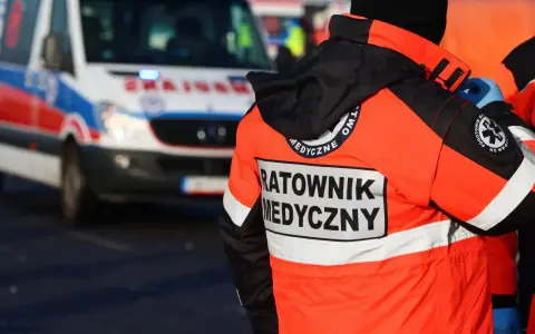 Ratownik medyczny w pomarańczowej kurtce z napisem "RATOWNIK MEDYCZNY" obok karetki. Zastanawiasz się, ile zarabia ratownik medyczny?