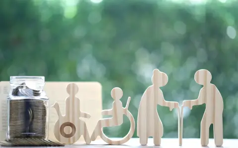 Skarbonka i drewniane figurki symbolizujące wsparcie dla osoby z niepełnosprawnością i seniorów.