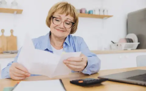 Uśmiechnięta starsza pani z okularami przegląda dokumenty, być może związane z rentą socjalną z MOPS.