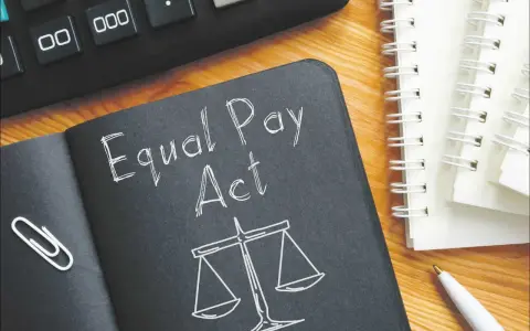 Notatnik z napisem "Equal Pay Act" i wagą sprawiedliwości symbolizuje jawność wynagrodzeń. Obok kalkulator i długopis.