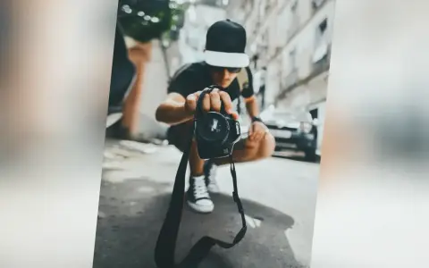 Młody fotograf w czapce z daszkiem trzyma aparat, zastanawiając się, ile zarabia fotograf w dzisiejszych czasach.