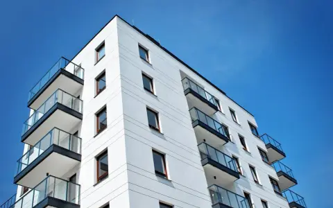 Nowoczesny budynek mieszkalny z balkonami i szklanymi balustradami, na tle błękitnego nieba. Idealne miejsce do życia, jak w pit 39.