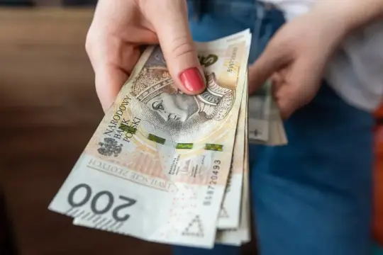Dłoń trzyma stos banknotów 200 zł. Czekamy na przelew, kiedy ZUS robi przelewy, to zawsze radość.