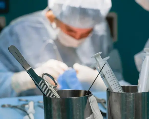 Chirurgowie w akcji. Zastanawiasz się, ile zarabia lekarz? W tle widać zespół medyczny podczas operacji, a na pierwszym planie narzędzia chirurgiczne i strzykawki.
