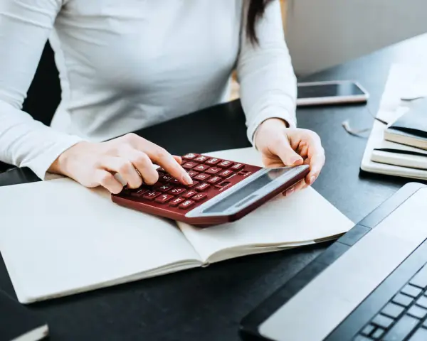 Kobieta liczy wydatki na własne cele mieszkaniowe, przygotowując PIT-39. Na biurku notatnik, kalkulator i laptop.
