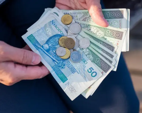 Ręce trzymają polskie banknoty i monety. Czy mam 60 lat i 10 lat pracy, czy dostanę emeryturę?
