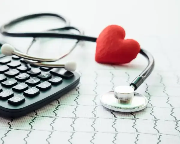 Stetoskop, kalkulator i czerwone serce na tle EKG symbolizują troskę o zdrowie i planowanie finansowe, w tym dobrowolne ubezpieczenie chorobowe.