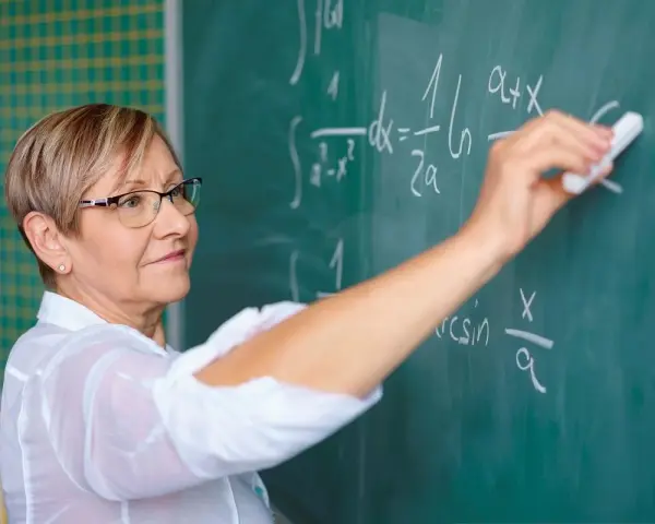 Nauczyciel początkujący pisze kredą wzory matematyczne na tablicy.