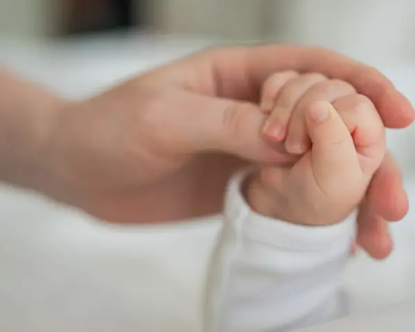 Dłoń rodzica obejmuje maleńką dłoń dziecka. To symbol miłości i wsparcia, jak świadczenie rodzicielskie.
