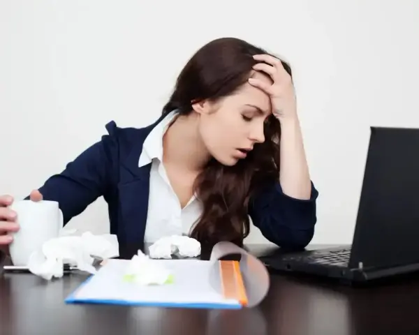 Zmęczona kobieta z kubkiem i chusteczkami przy laptopie. Zastanawia się, ile można być na zwolnieniu lekarskim od psychiatry.
