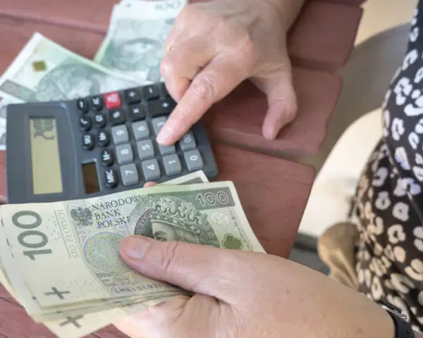 Ręce liczą banknoty 100 zł przy kalkulatorze. Może to być pomocne przy analizie nowych zasad przejścia na emeryturę tabela.