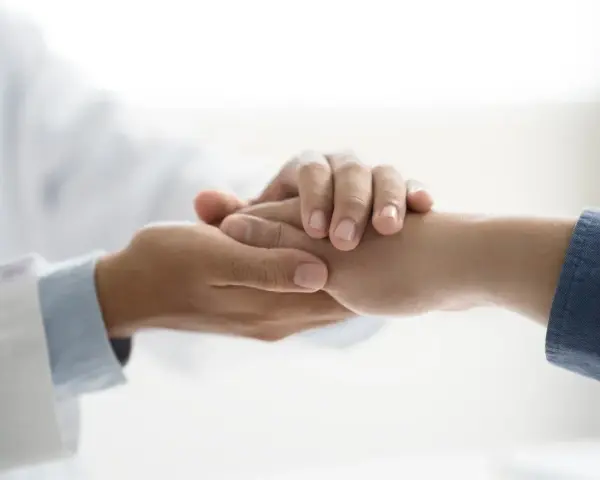Lekarz w białym kitlu trzyma dłoń pacjenta, okazując wsparcie. To symbol troski i nadziei, ważny dla osób z niepełnosprawnością.