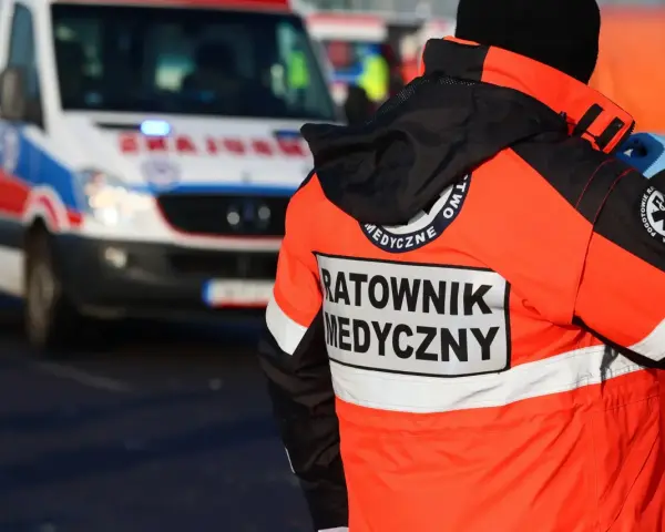 Ratownik medyczny w pomarańczowej kurtce z napisem "RATOWNIK MEDYCZNY" obok karetki. Zastanawiasz się, ile zarabia ratownik medyczny?