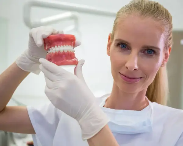 Dentystka w białej rękawiczce pokazuje model szczęki z aparatem ortodontycznym. Zastanawiasz się, ile zarabia dentysta?