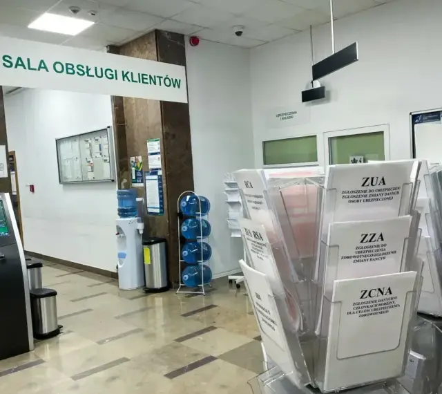 Sala obsługi klienta z terminalem, dystrybutorem wody i stojakami z formularzami ZUS, np. ZUA, ZZA, ZCNA. rp7.