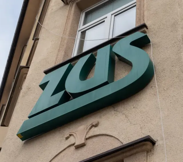 Zielone logo ZUS na budynku. To miejsce, gdzie można załatwić sprawy związane z ubezpieczeniem chorobowym.