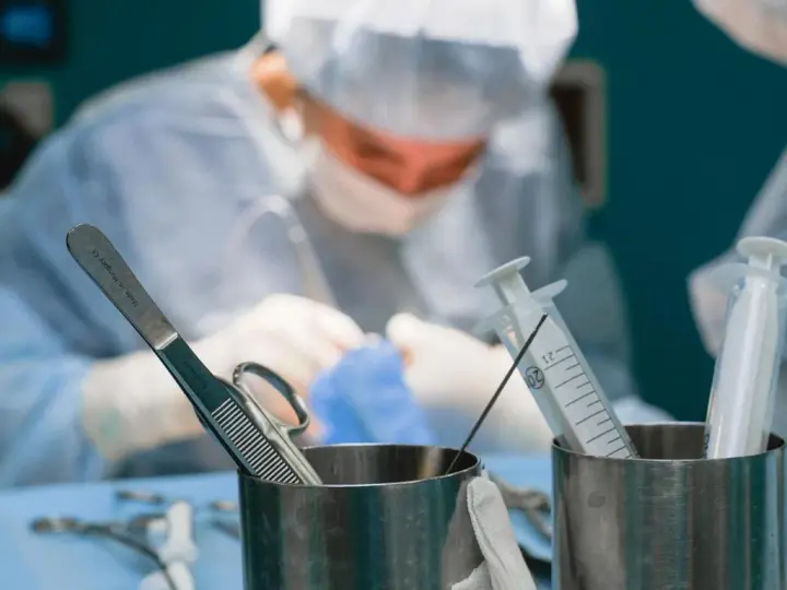 Chirurgowie w akcji. Zastanawiasz się, ile zarabia lekarz? W tle widać zespół medyczny podczas operacji, a na pierwszym planie narzędzia chirurgiczne i strzykawki.