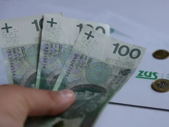 Trzy stuzłotowe banknoty w dłoni, obok dokument ZUS i monety. Czy to zapowiedź 30 krotności ZUS 2025?