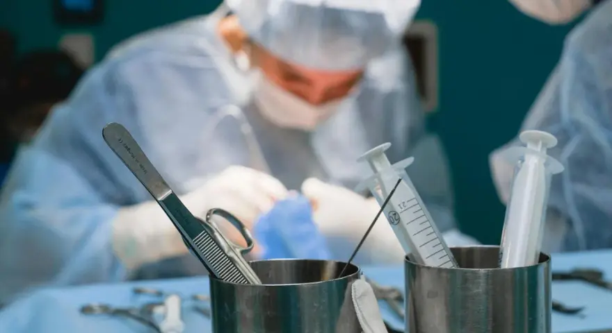 Chirurgowie w akcji. Zastanawiasz się, ile zarabia lekarz? W tle widać zespół medyczny podczas operacji, a na pierwszym planie narzędzia chirurgiczne i strzykawki.