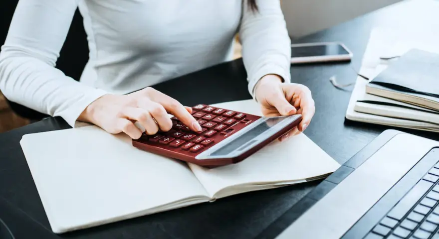 Kobieta liczy wydatki na własne cele mieszkaniowe, przygotowując PIT-39. Na biurku notatnik, kalkulator i laptop.