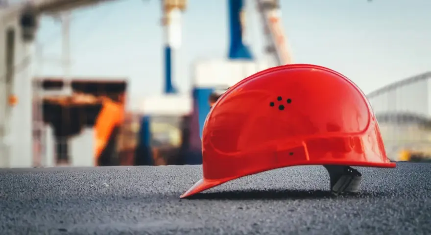 Czerwony kask budowlany na tle placu budowy. Symbol bezpieczeństwa pracy, który może wpływać na stopę procentową składek na ubezpieczenie wypadkowe.