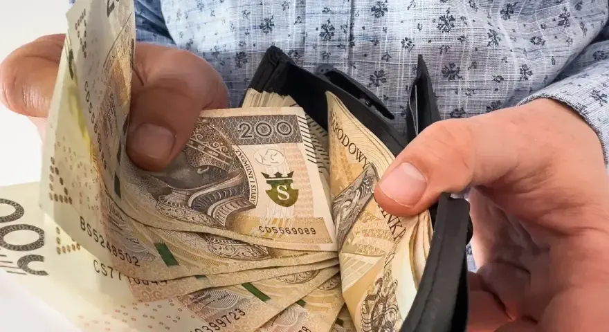 Ręce trzymają portfel z banknotami 200 zł. Czy to zapowiedź trzynastki w 2026 roku?