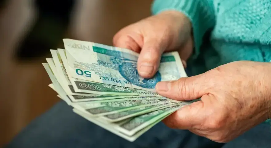 Dłonie starszej osoby liczą banknoty. Zastanawiasz się, ile wynosi dodatek do emerytury za warunki szkodliwe?