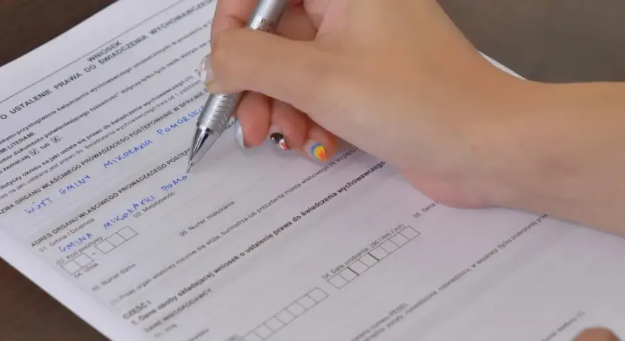 Ręka wypełnia kwestionariusz osobowy, wpisując dane dotyczące świadczenia wychowawczego.