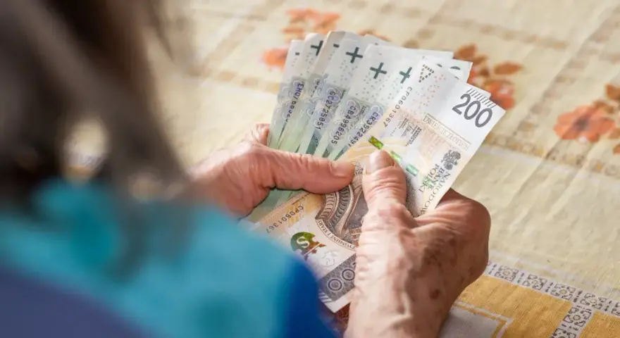 Dłonie starszej osoby liczą banknoty 200 zł. Tabela 14. emerytury może zawierać takie kwoty.