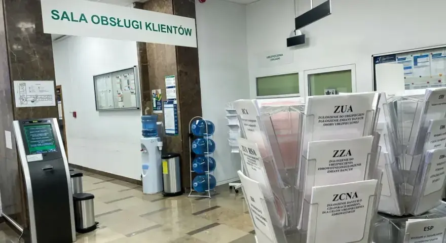 Sala obsługi klienta z terminalem, dystrybutorem wody i stojakami z formularzami ZUS, np. ZUA, ZZA, ZCNA. rp7.