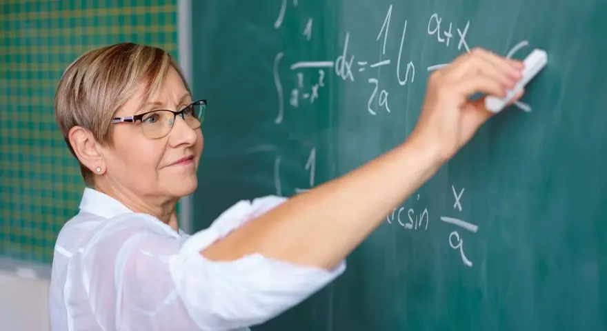 Nauczyciel początkujący pisze kredą wzory matematyczne na tablicy.