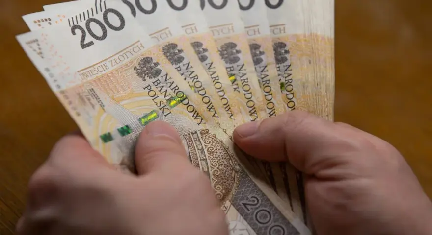 Dłonie trzymają stos banknotów po 200 zł. Czy to wystarczy, by poznać, ile wynosi najniższa krajowa netto?