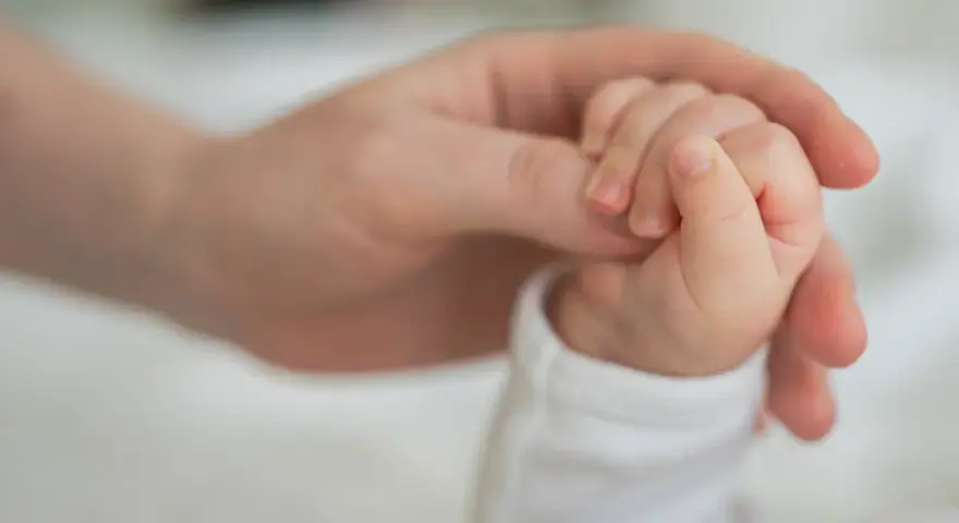 Dłoń rodzica obejmuje maleńką dłoń dziecka. To symbol miłości i wsparcia, jak świadczenie rodzicielskie.
