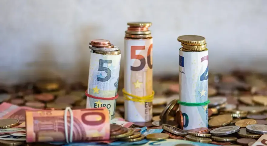 Zwijane banknoty euro i monety, symbolizujące kwotę darowizny wolną od podatku, tworzą stosy na tle innych monet.