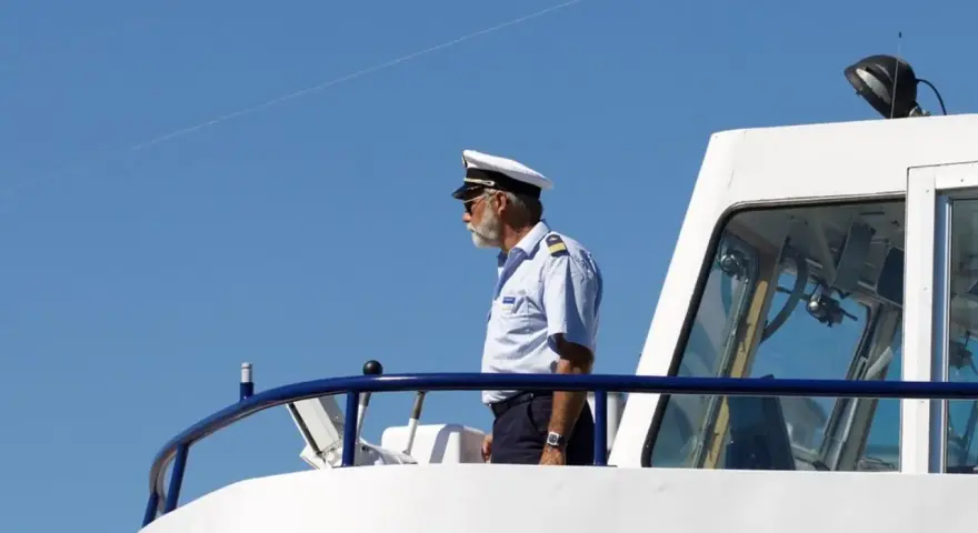 Kapitan na mostku statku, w białym mundurze i czapce, spogląda w dal. Zastanawiasz się, ile zarabia marynarz?