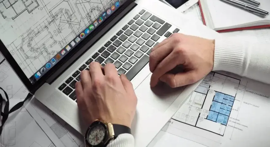 Architekt pracuje nad projektem na laptopie, analizując plany. Zastanawiasz się, ile zarabia architekt?