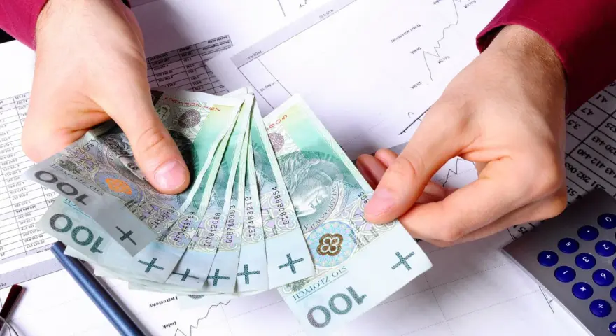 Ręce trzymające polskie stuzłotówki, obok kalkulator i wykresy. Jak wypłacić pieniądze z PPK?