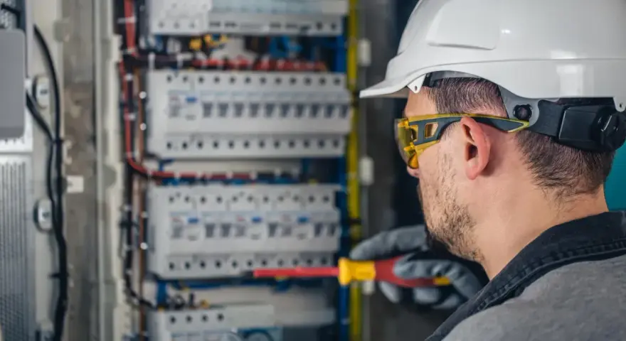Elektryk w kasku i okularach ochronnych pracuje przy rozdzielnicy. Zastanawiasz się, ile zarabia elektryk?