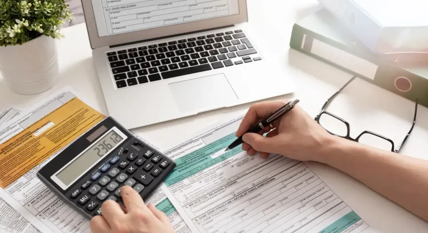 Ręce wypełniające formularz PIT-37, obok kalkulatora z wynikiem 236.12, laptopa i okularów.