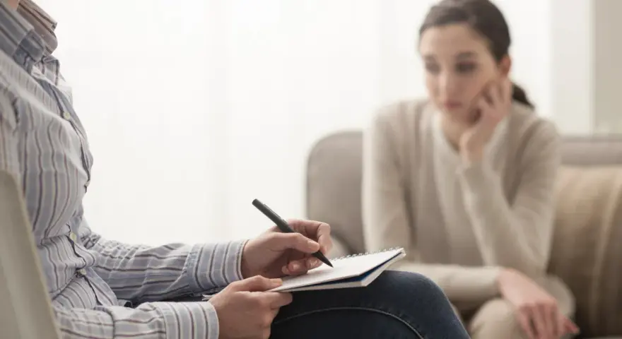 Psycholog notuje, analizując sytuację pacjentki. Zarobki psychologa zależą od doświadczenia i specjalizacji.