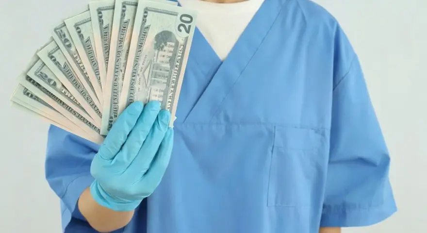 Higienistka stomatologiczna w niebieskim fartuchu pokazuje wachlarz banknotów 20 dolarowych. Zastanawiasz się, ile zarabia higienistka stomatologiczna?
