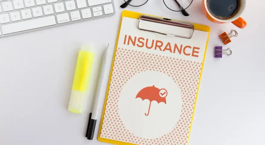 Dokument "Insurance" z parasolką, klawiatura, okulary, kawa. Planowanie ubezpieczenia zdrowotnego bez pracy.
