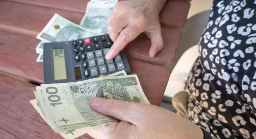 Ręce liczą banknoty 100 zł przy kalkulatorze. Może to być pomocne przy analizie nowych zasad przejścia na emeryturę tabela.
