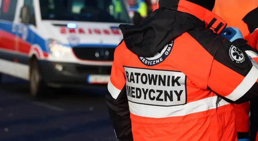 Ratownik medyczny w pomarańczowej kurtce z napisem "RATOWNIK MEDYCZNY" obok karetki. Zastanawiasz się, ile zarabia ratownik medyczny?