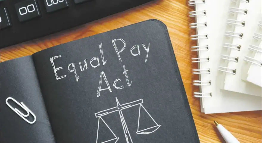 Notatnik z napisem "Equal Pay Act" i wagą sprawiedliwości symbolizuje jawność wynagrodzeń. Obok kalkulator i długopis.