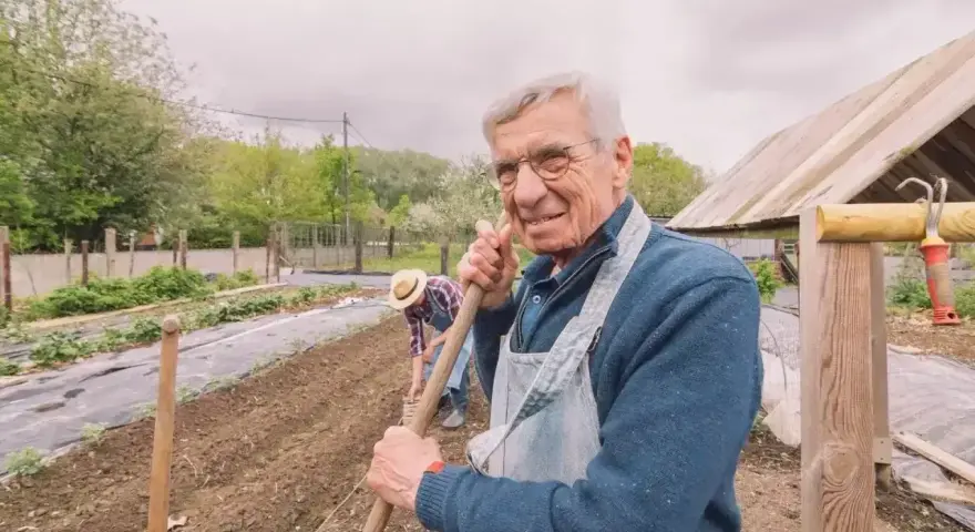 Uśmiechnięty starszy pan z łopatą w ręku, pracujący w ogrodzie. Zastanawia się, jaka emerytura z KRUS po 10 latach będzie mu przysługiwać.