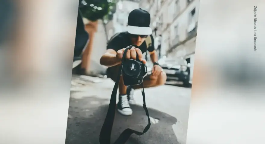 Młody fotograf w czapce z daszkiem trzyma aparat, zastanawiając się, ile zarabia fotograf w dzisiejszych czasach.